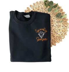 Our new Spooky Season Halloween Sweatshirt is the perfect addition to your Fall and Halloween wardrobe. This embroidered sweatshirt is professionally embroidered and will definitely get you excited for Fall and Halloween!  Professionally embroidered with left chest placement.  Sweatshirt is a 8 oz. 50/50 cotton/polyester blend fleece Spooky season will be embroidered with our premium orange thread. The ghost will be embroidered with black thread on the following colors - White, Sand, Light Blue, Black Embroidered T-shirt For Fall, Custom Embroidered Long Sleeve Top For Halloween, Black Fall Sweater With Embroidered Text, Black Sweater With Embroidered Text For Fall, Black Embroidered Text Sweater For Fall, Black Embroidered Tops For Halloween, Black Sweatshirt With Custom Embroidery For Fall, Black T-shirt With Custom Embroidery For Fall, Black Embroidered Sweater For Fall