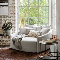 a living room filled with furniture next to a brick wall and large window overlooking trees