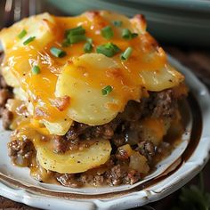 a white plate topped with potatoes and meat covered in cheese on top of a wooden table