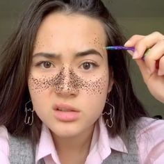 a woman with black dots on her face is holding a pencil and looking at the camera