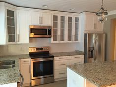 a kitchen with stainless steel appliances and granite counter tops, white cabinets, and marble counters