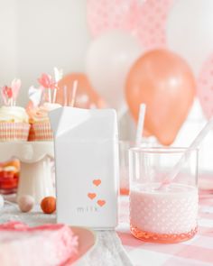 a pink and white table topped with lots of cupcakes next to a milk carton