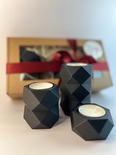 three black candles sitting next to each other in front of a box with a red ribbon