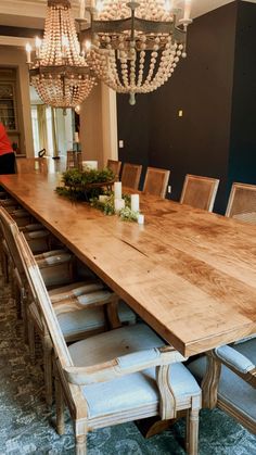 a large wooden table surrounded by chairs with chandeliers hanging from it's ceiling