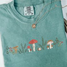 a t - shirt with embroidered mushrooms on the front and back, sitting next to scissors