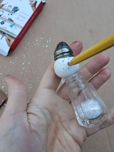 a person holding a small glass bottle with a snowman inside and a pencil sticking out of it