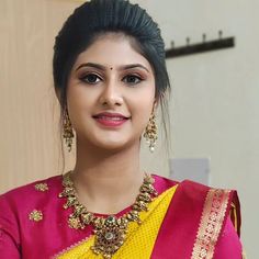 a woman in a pink and yellow sari with gold jewelry on her neck, smiling at the camera