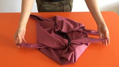 a woman is making something out of purple material on an orange table top with her hands