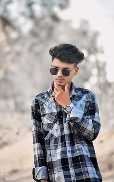 a young man wearing sunglasses standing in front of a rock formation with his hand on his chin