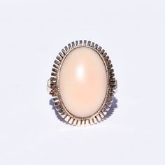 A charming angel skin coral ring in 8k gold. Features a large pink cabochon mounted in a bezel setting with a stylized cutout trim. The design is simple yet striking, and the ring would make a fabulous addition to an estate jewelry collection. The gold has an antique patina with some surface scuffs, and the cabochon remains secure in its setting. The inner band is hallmarked '8K', and the gold has been tested for authenticity. In good vintage condition with age-appropriate wear and discoloration.  **This listing contains photographs of the actual item you will receive. Please look closely at the pictures, which are part of the product description. Every piece is cleaned, polished, examined, and described to the best of our ability, and we encourage you to reach out with any questions.** Co Classic Pink Cabochon Jewelry, Classic Pink Cabochon Rings, Elegant Pink Oval Cabochon Ring, Elegant Pink Cabochon Rings, Vintage Pink Cabochon Ring, Pink Oval Cabochon Opal Ring, Classic Pink Oval Cabochon Ring, Elegant Pink Opal Ring For Formal Occasions, Formal Pink Oval Opal Ring