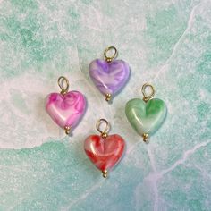 three heart shaped charms sitting on top of a green and white surface with gold bails