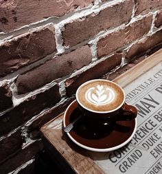 a cappuccino sitting on top of a wooden table next to a brick wall