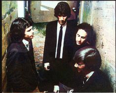 four men in suits and ties are talking to each other while one man looks at something on the ground