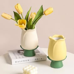 two vases with flowers in them sitting on a table next to an open book