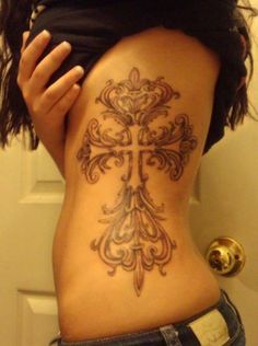 a woman with a cross tattoo on her lower back is standing in front of a door