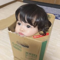 a small child in a cardboard box with her head sticking out from the top of it