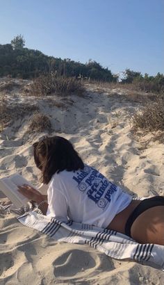 a woman laying in the sand reading a book