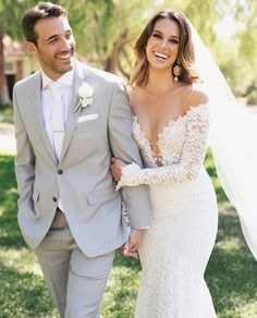 a bride and groom holding hands walking through the grass in their wedding day attire, smiling at each other