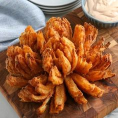 some fried food is sitting on a cutting board next to bowls of dips and sauce