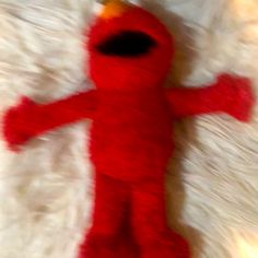 a red stuffed animal laying on top of a white fur covered floor next to a wall