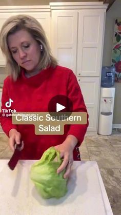 a woman in a red sweater is cutting lettuce on a white counter top