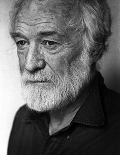 an old man with a long white beard wearing a black shirt and looking at the camera