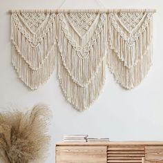 three macrame wall hangings on the wall next to a dresser and plant