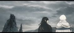 two people standing on top of a mountain under a cloudy sky with mountains in the background