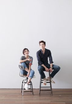 two people sitting on chairs in front of a white wall