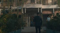 two men in suits are walking towards a building with balconies on the second floor