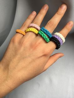 a person's hand with four different colored braided rings on their fingers,