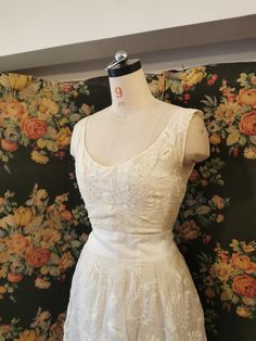 a white dress on a mannequin in front of a floral wall