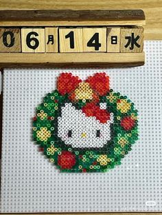 a cross stitch hello kitty christmas ornament hanging from a wooden frame on a wall