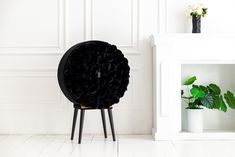 a black chair sitting in front of a white wall with flowers on it and a potted plant next to it