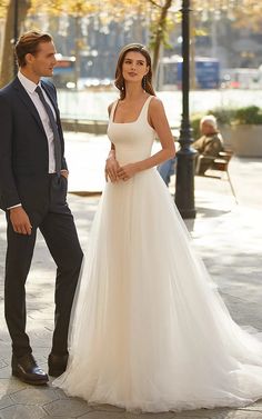 a man and woman standing next to each other in front of a street light wearing wedding gowns