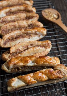 several sausages on a grill with a wooden spoon next to them and another dish in the background