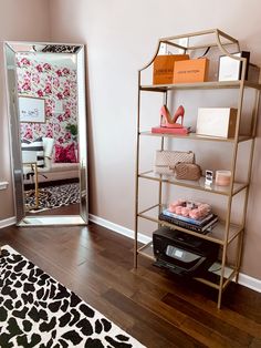 a living room with pink walls and wooden flooring, a gold shelving unit filled with books