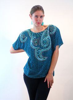 "This is a gorgeous 80s vintage beaded and sequined silk top! It is a rich teal ocean green shade with an elaborate floral and swirl design on the front made with iridescent green sequins, metallic bugle beads and faux pearl beads. Shimmering green bugle beads create an allover squiggle design on the rest of the front, the back and the sleeves. It has short sleeves edged with beadwork, a straight hem with bead trim, and large shoulder pads which could be removed, if desired. The top is fully lin Beaded Top For Spring Party, Spring Party Beaded Top, Fitted Beaded Tops For Festival, Glamorous Beaded Tops For Party Season, Fitted Bohemian Beaded Tops, Glamorous Sequined Tops For Festivals, Beaded Short Sleeve Top For Party, Bohemian Beaded Tops For Night Out, Festive Beaded Tops For Night Out