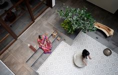 two women are sitting on the floor in front of a plant and looking down at something