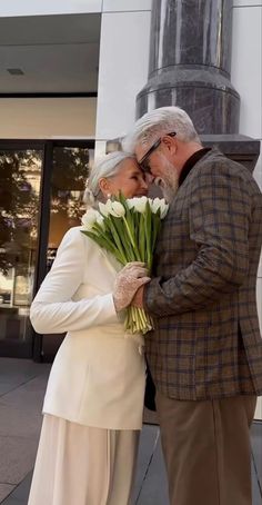 an older couple embracing each other in front of a building