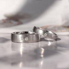 two wedding rings sitting on top of a white table next to each other with diamonds in them