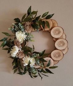 a wreath made out of wood slices with white flowers and greenery on top is hung on the wall