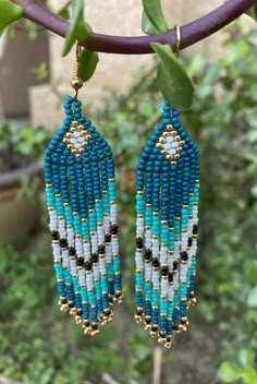 blue and white beaded earrings hanging from a tree branch in front of green leaves