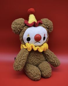 a brown teddy bear with a clown mask on it's face and nose sitting in front of a red background