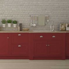 a kitchen with red cabinets and white brick wall behind the countertop is filled with potted plants