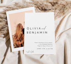 the wedding announcement card is laying on top of a white bed sheet with fur trimming