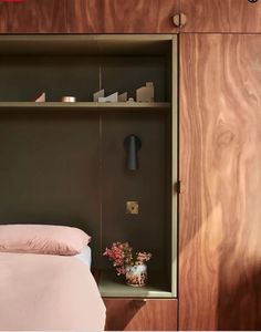 a bed sitting under a wooden shelf next to a lamp and vase with flowers on it