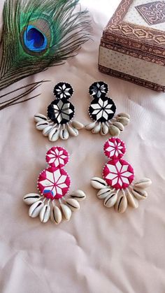 three pairs of earrings sitting on top of a bed next to a peacock's tail