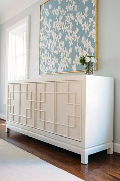 a white cabinet sitting on top of a hard wood floor next to a large painting