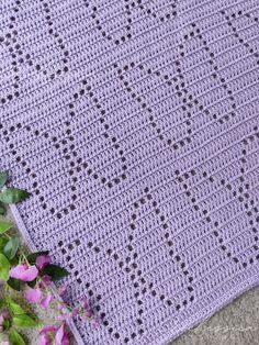 a purple crocheted blanket laying on the ground next to flowers